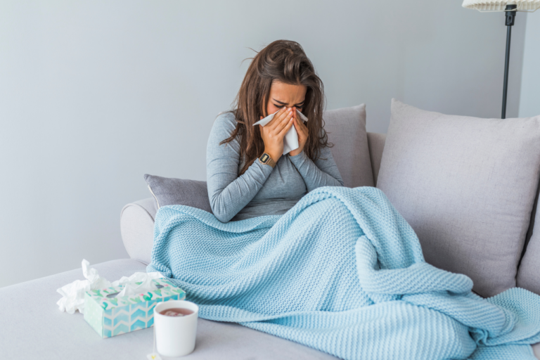 Mujer joven sonándose la nariz tapada con una manta